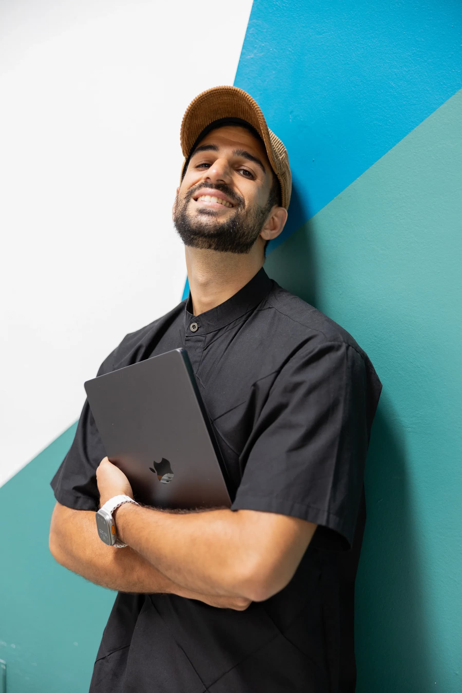 Aaron Ullal, fondatore di Diafonis, appoggiato a una parete dipinta con un portatile sottobraccio, sorridente